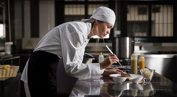 Junge Köchin steht in einer Restaurantküche und richtet ein Steak an