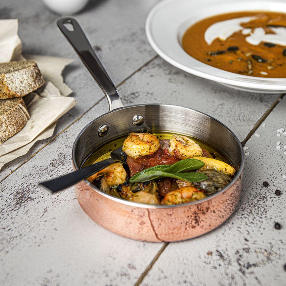 Garnelengericht in Kupferpfännchen und Kürbissuppe mit Brot auf einem Tisch